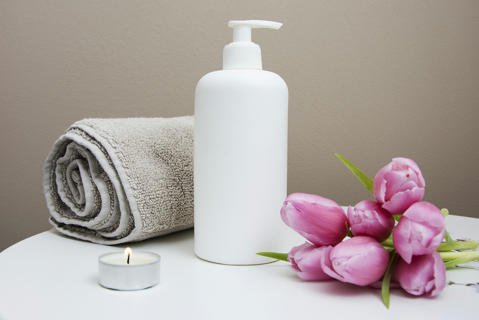 White pump bottle beside pink tulips and a folded gray towel