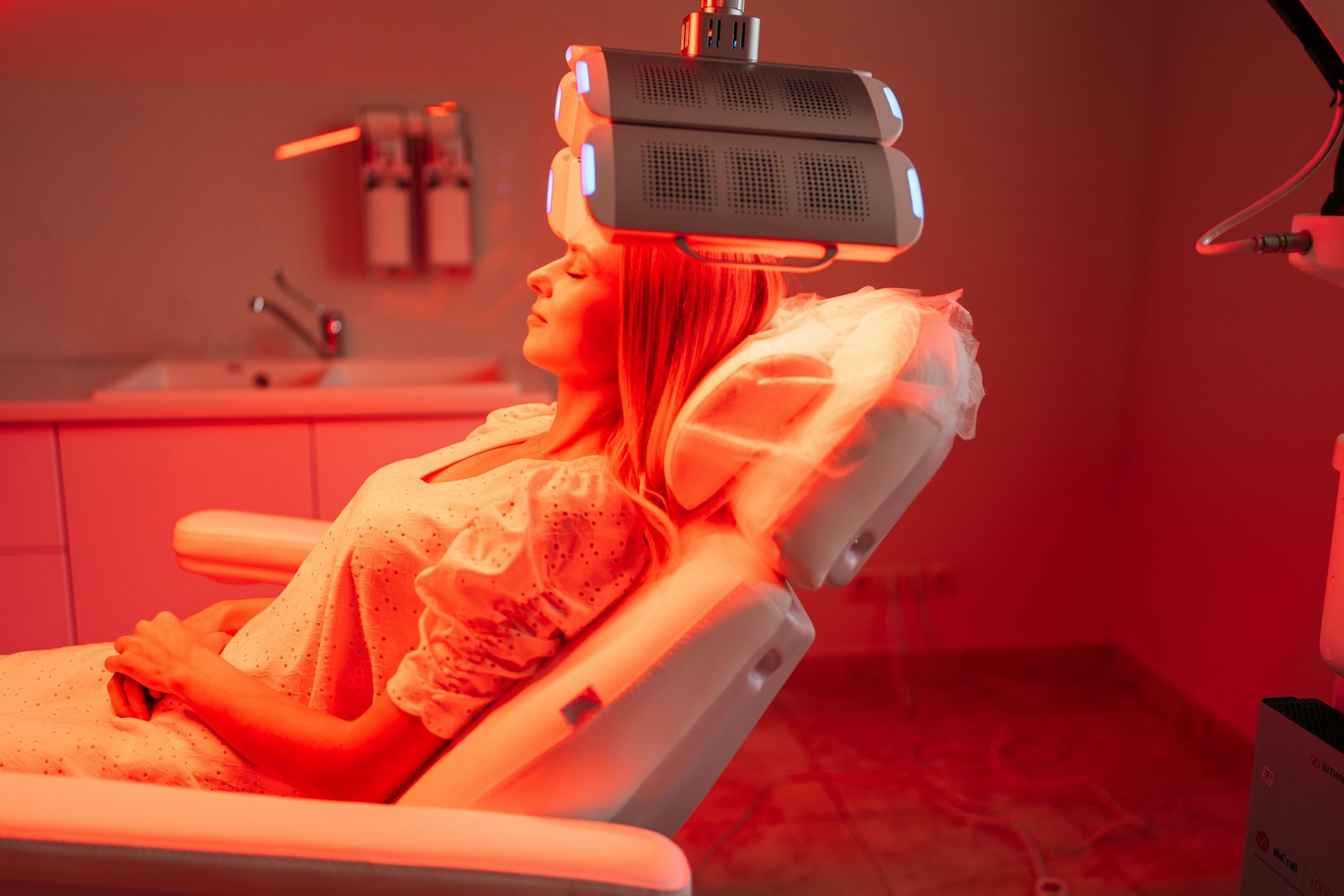Woman reclining in a treatment chair beneath an LED red light panel