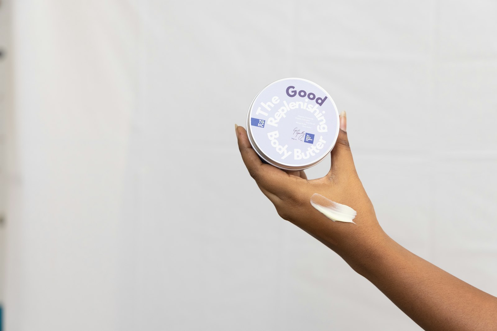 Hand holding an open jar of cream with a smear of it on the skin