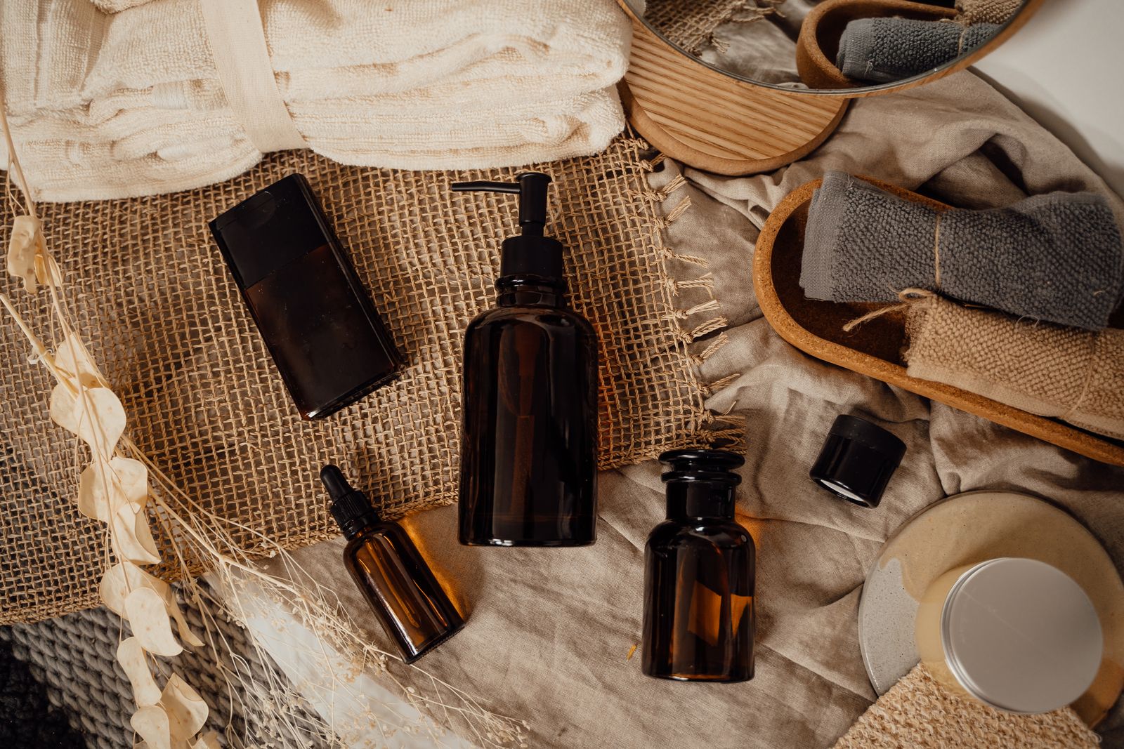 Skincare and body care bottles arranged with dried flowers and towels